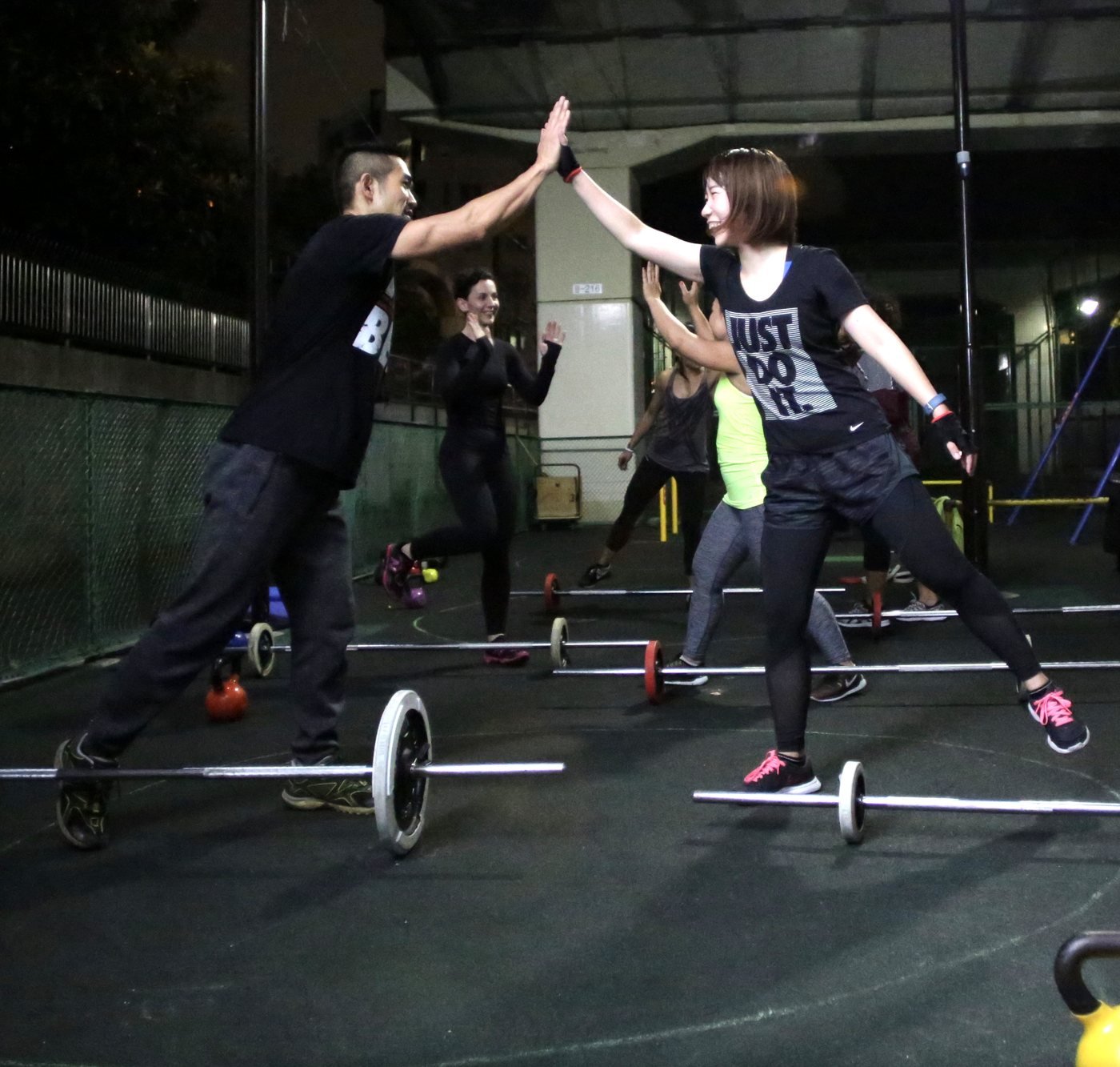 Members high-fiving over barbells during a warm-up game